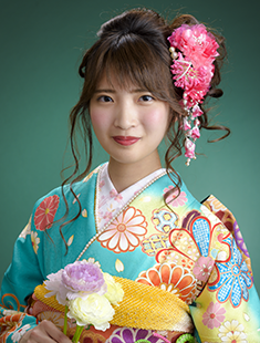 緑の背景で花を持ち微笑む振袖写真