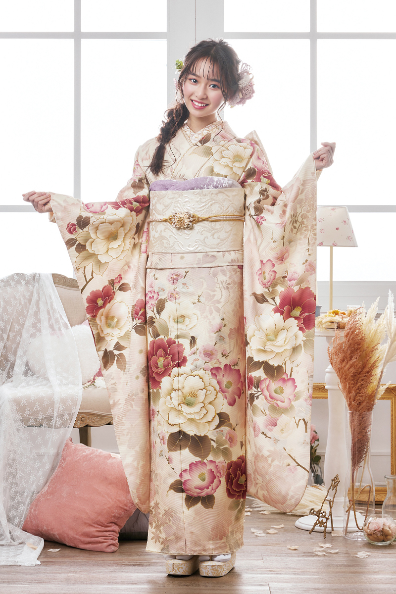 淡いアイボリーピンクに大ぶりの八重桜が優しく舞う振袖。明るいスタジオ光に包まれた、二十歳のピュアな美しさと笑顔が輝くスタイル。